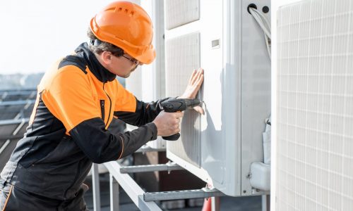 Professional workman in protective clothing installing or reparing outdoor unit of the air conditioner or heat pump on the rooftop